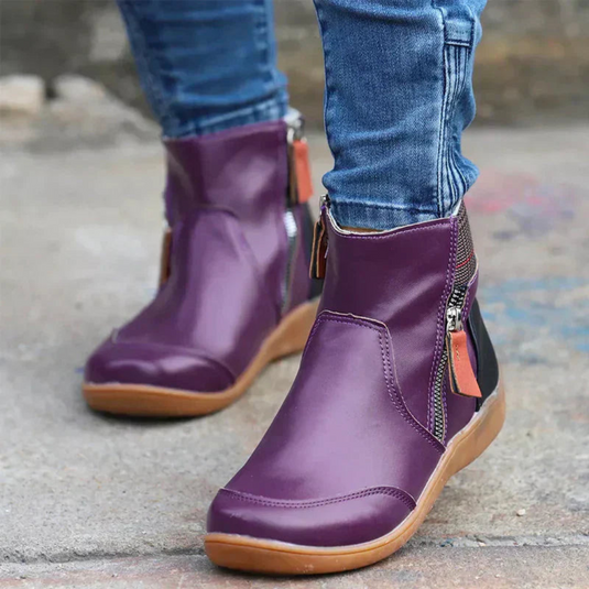 Lila Damenstiefeletten mit Reißverschluss, kombiniert mit blauen Jeans. Modische, bequeme Schuhe für Herbst und Winter. Straßenhintergrund.