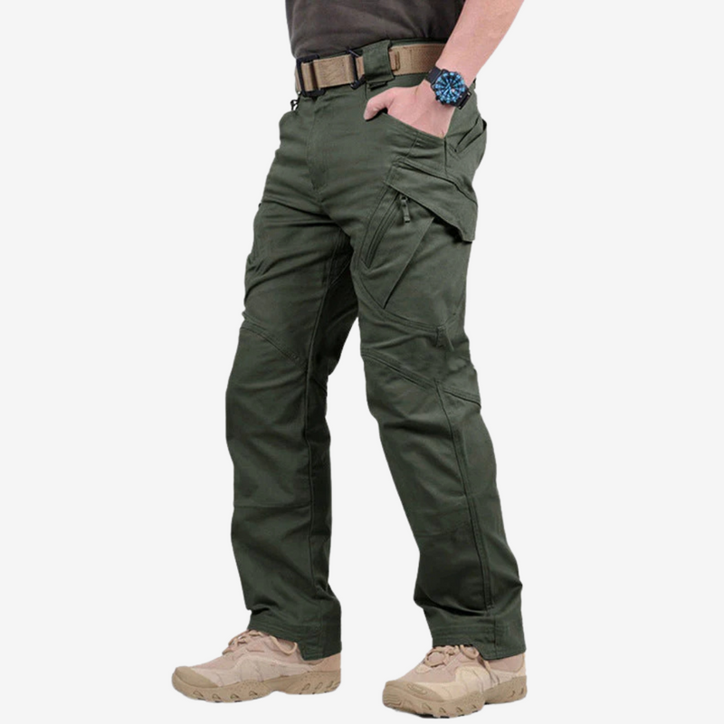 Laden Sie das Bild in Galerie -Viewer, Mann trägt grüne taktische Hose mit mehreren Taschen, beigen Stiefeln und einer Armbanduhr. Outdoor-Bekleidung, funktionale Mode, robuste Hosen.
