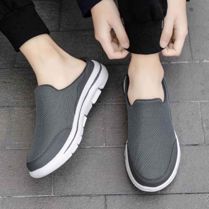 Laden Sie das Bild in Galerie -Viewer, Graue Slip-On-Sneaker mit weißer Sohle auf grauem Pflaster, Hände binden Hosenbein. Bequeme, atmungsaktive Freizeitschuhe für Herren.
