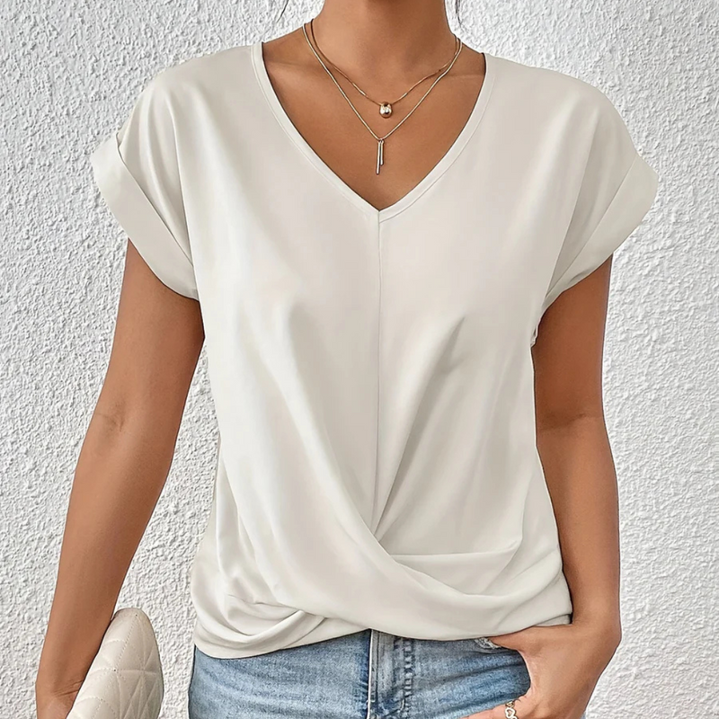 Laden Sie das Bild in Galerie -Viewer, Frau trägt elegantes, weißes V-Ausschnitt-Shirt mit kurzen Ärmeln und Knoten-Detail, kombiniert mit blauer Jeans. Perfekt für Sommermode und Freizeitlook.
