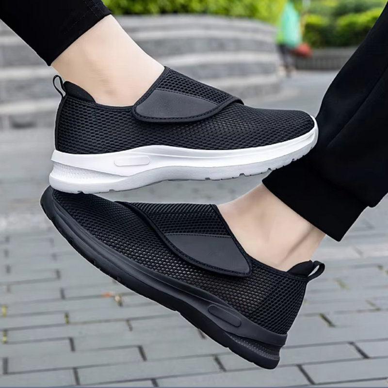 Laden Sie das Bild in Galerie -Viewer, Schwarze, atmungsaktive Slip-On-Sneaker mit weißer Sohle auf grauem Pflaster. Bequeme Freizeitschuhe für Damen und Herren, ideal für den Alltag.
