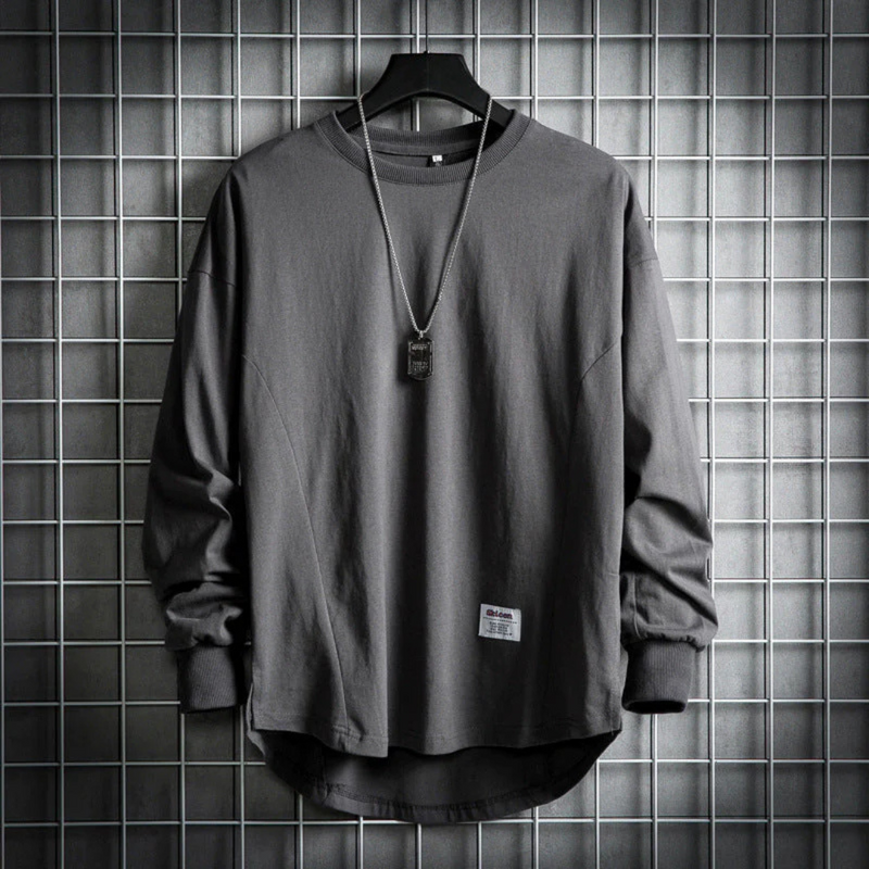Laden Sie das Bild in Galerie -Viewer, Graues Langarmshirt auf Kleiderbügel vor Gitterwand, lässiger Stil, Rundhalsausschnitt, mit Kette. Modetrend, Herrenbekleidung, urbaner Look.
