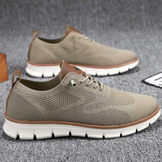 Beige Herren-Sneaker aus atmungsaktivem Strickgewebe mit weißer Sohle, ideal für Freizeit und Sport. Moderne, leichte Schuhe auf grauem Hintergrund.