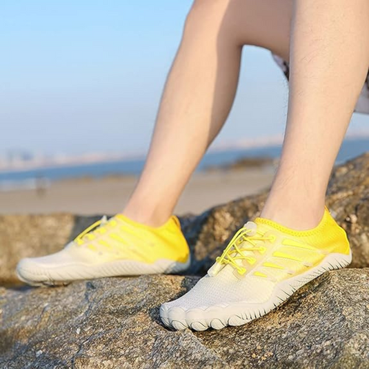 Gelbe Barfußschuhe auf Felsen am Strand, ideal für Outdoor-Aktivitäten. Leichte, atmungsaktive Sportschuhe für Sommer und Freizeit.