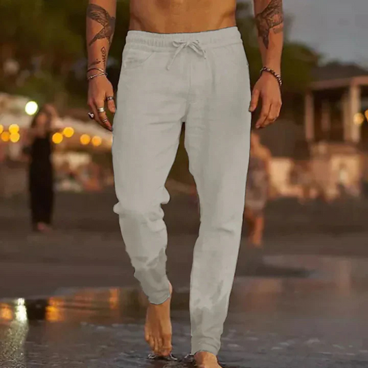 Barfuß laufender Mann in grauer Jogginghose am Strand bei Sonnenuntergang. Freizeitmode, Strandspaziergang, entspannte Atmosphäre.