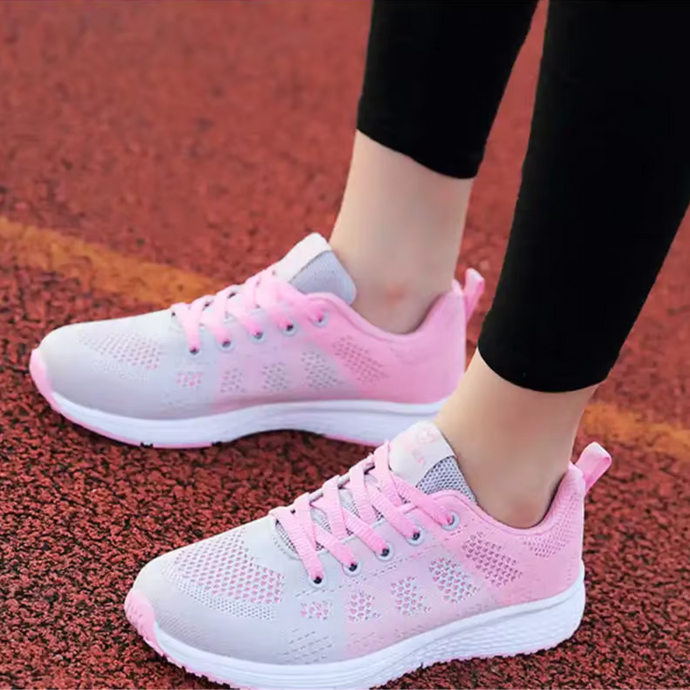 Damen Sneaker in Rosa und Weiß auf rotem Laufbahn-Belag. Bequeme Sportschuhe, ideal für Laufen und Fitness. Trendige, atmungsaktive Turnschuhe.