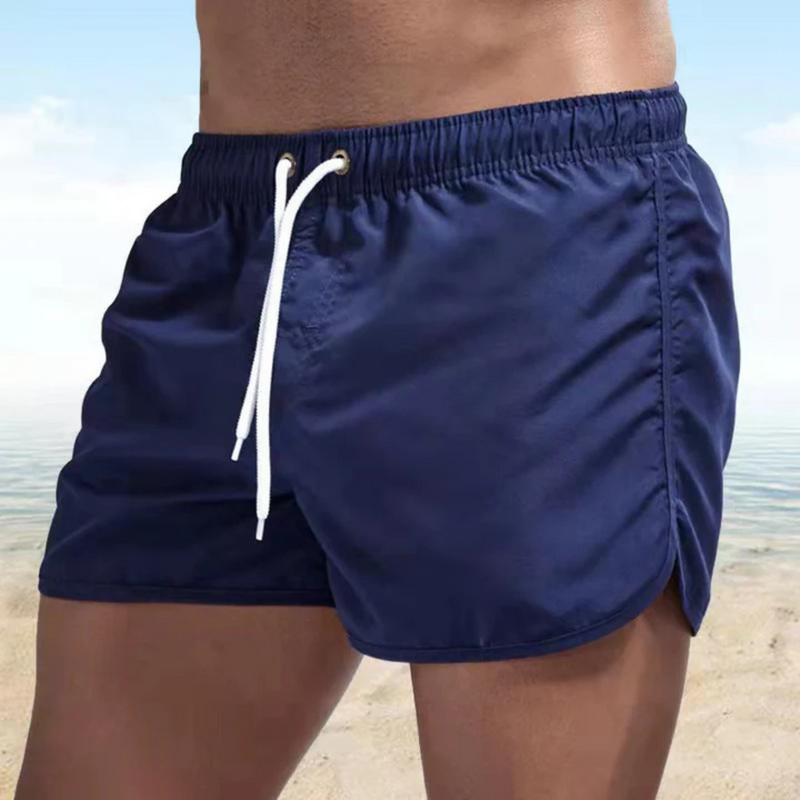 Laden Sie das Bild in Galerie -Viewer, Mann in blauer Badehose am Strand, Sommermode, Herren-Bademode, Strandbekleidung, sportlich, Meereshintergrund, Freizeitkleidung.
