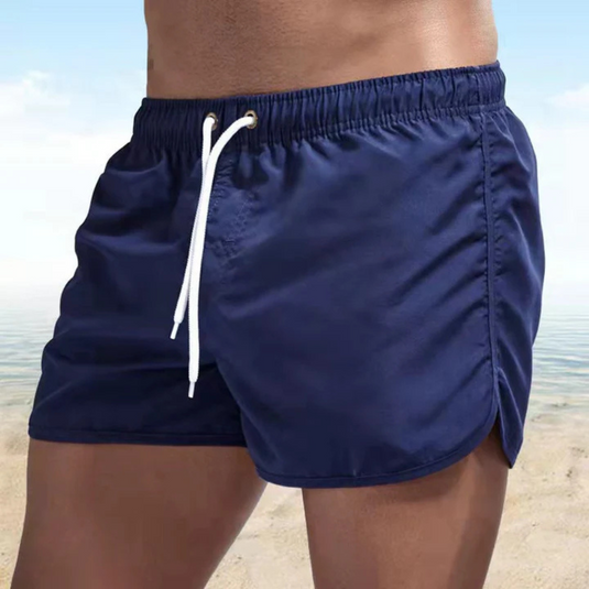 Mann in blauer Badehose am Strand, Sommermode, Herren-Bademode, Strandbekleidung, sportlich, Meereshintergrund, Freizeitkleidung.