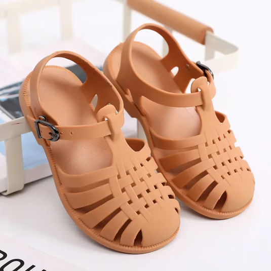 Braune Sandalen aus Kunststoff mit Riemen und Schnalle auf weißem Hintergrund. Modische Sommerschuhe, ideal für Strand und Freizeit.