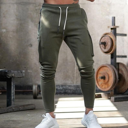 Grüne Jogginghose im Fitnessstudio, kombiniert mit weißen Turnschuhen. Hantelbank und Gewichte im Hintergrund. Sportmode, Fitness, Herrenbekleidung.