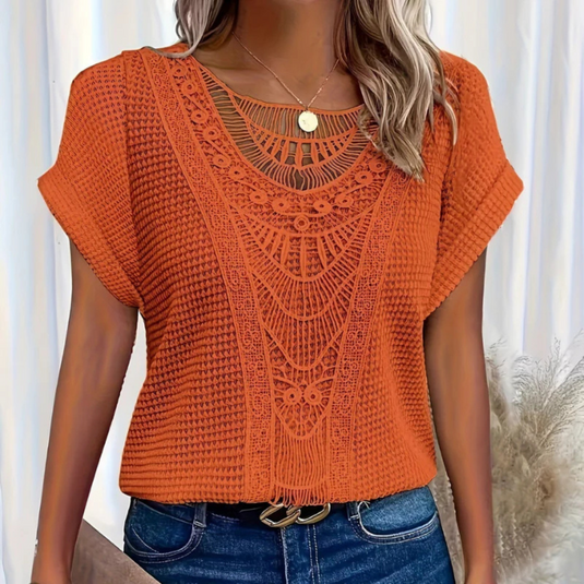 Frau trägt orangefarbenes, gehäkeltes Oberteil mit Spitzenmuster, kombiniert mit blauer Jeans. Modetrend, Sommermode, Damenbekleidung.