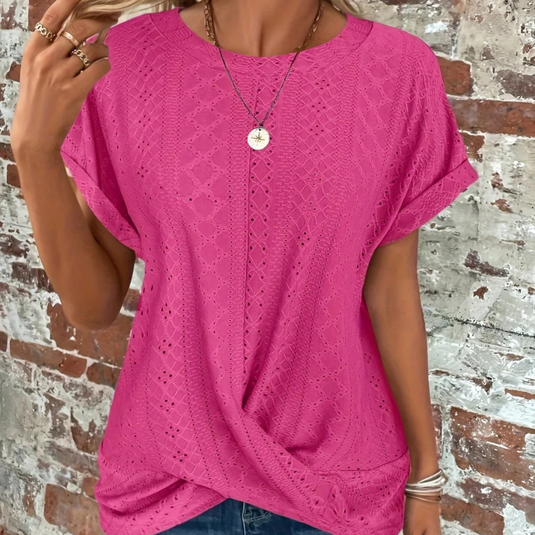 Frau trägt pinkes, gehäkeltes T-Shirt vor Backsteinwand, modisches Sommeroutfit, lässiger Stil, Schmuckaccessoires, trendige Damenmode.