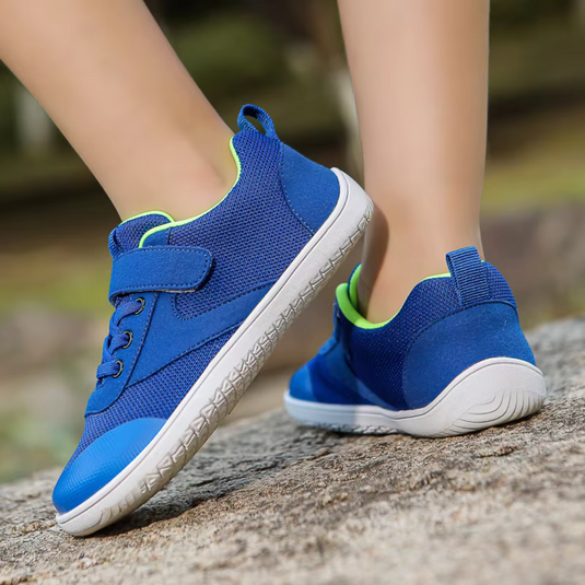 Blaue Kinderschuhe mit Klettverschluss und grünen Akzenten auf einem Steinweg. Bequeme, rutschfeste Sneakers für aktive Kinder.