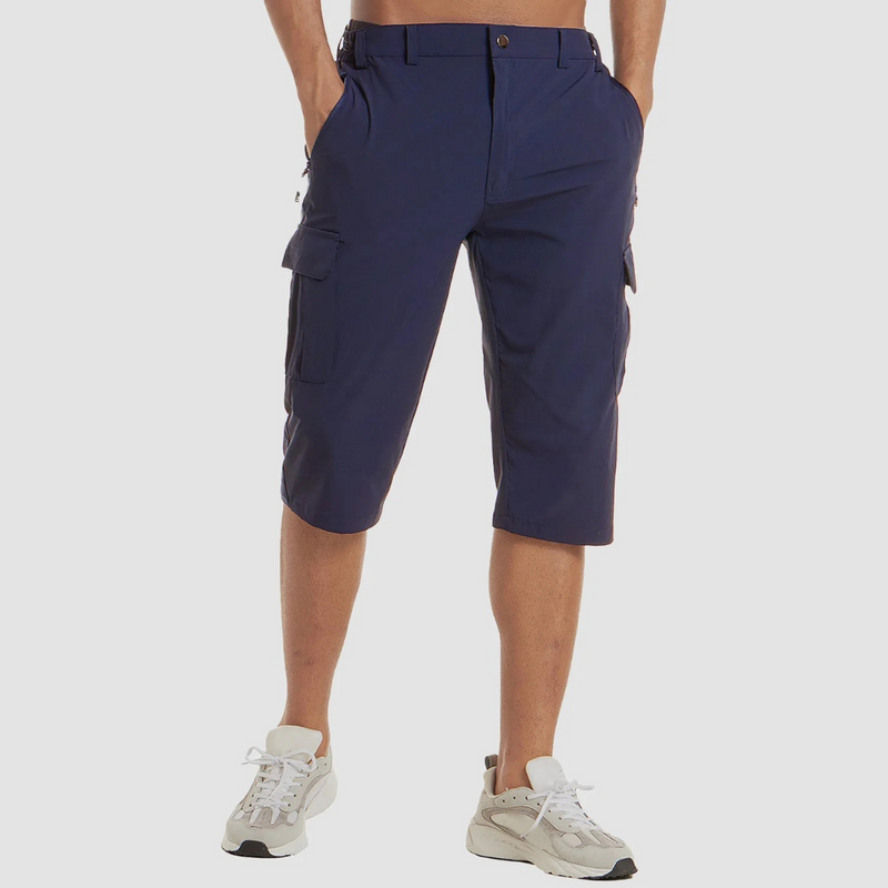 Laden Sie das Bild in Galerie -Viewer, Mann trägt dunkelblaue Cargo-Bermuda-Shorts und weiße Sneaker. Bequeme Sommermode, ideal für Freizeit und Outdoor-Aktivitäten.
