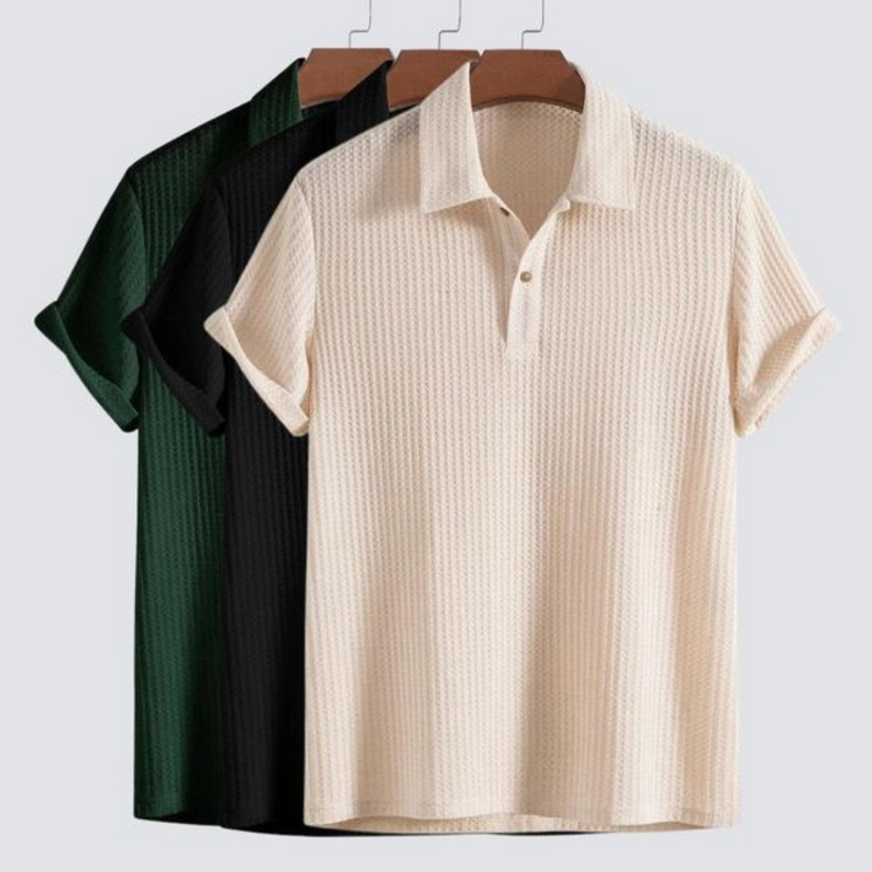 Laden Sie das Bild in Galerie -Viewer, Drei Poloshirts in Grün, Schwarz und Beige auf Kleiderbügeln vor grauem Hintergrund. Modische Herrenbekleidung, kurzärmelig, geripptes Design.

