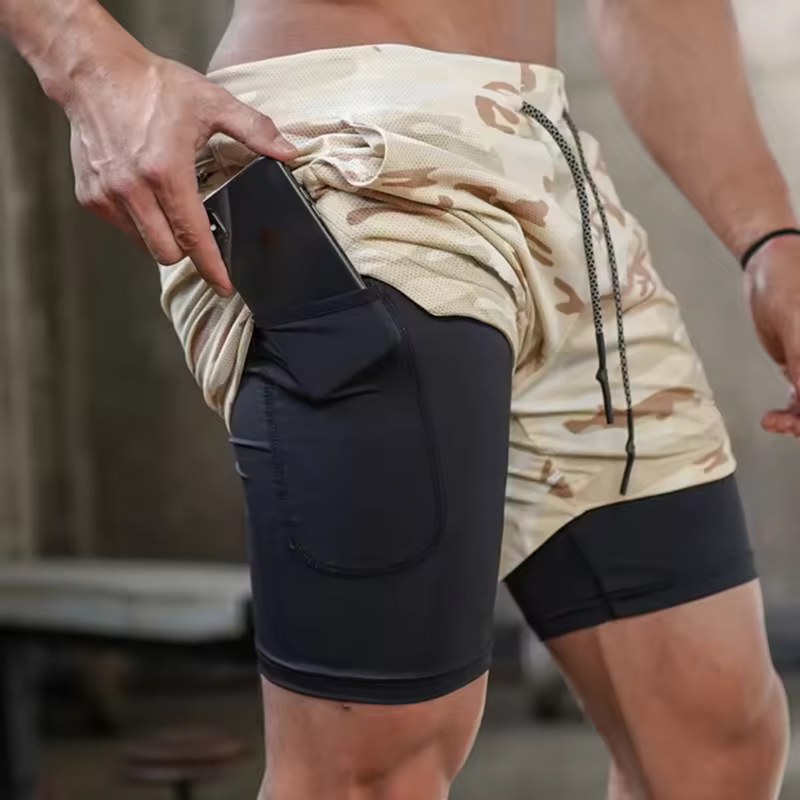 Laden Sie das Bild in Galerie -Viewer, Mann in Camouflage-Shorts mit integriertem Handyfach, Fitnessstudio-Hintergrund, Sportbekleidung, praktisches Design für Training und Outdoor-Aktivitäten.
