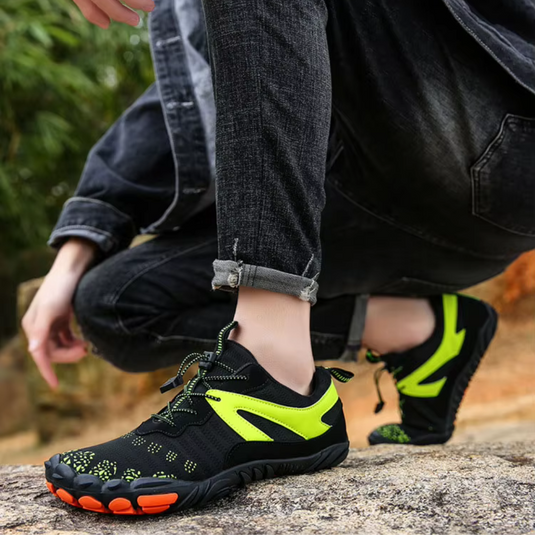 Schwarze und neon-gelbe Outdoor-Sportschuhe auf Naturpfad, getragen von Person in dunkler Jeans. Ideal für Wandern und Trailrunning.