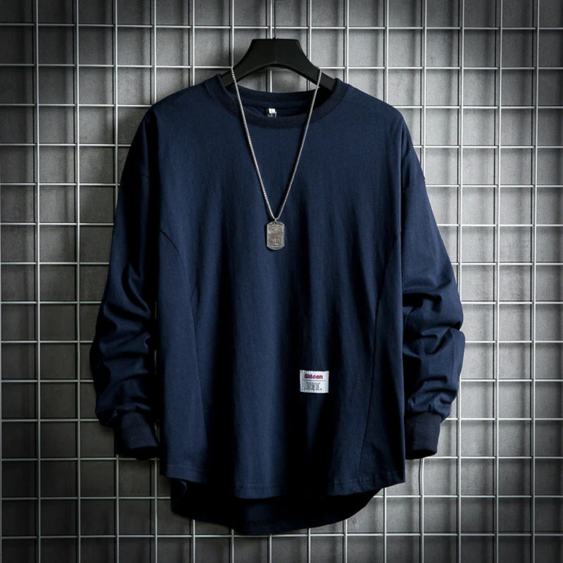 Laden Sie das Bild in Galerie -Viewer, Dunkelblaues Langarmshirt mit Kettenanhänger, hängend vor grauem Gitterhintergrund. Modisches Herrenoberteil, urbaner Streetwear-Stil.
