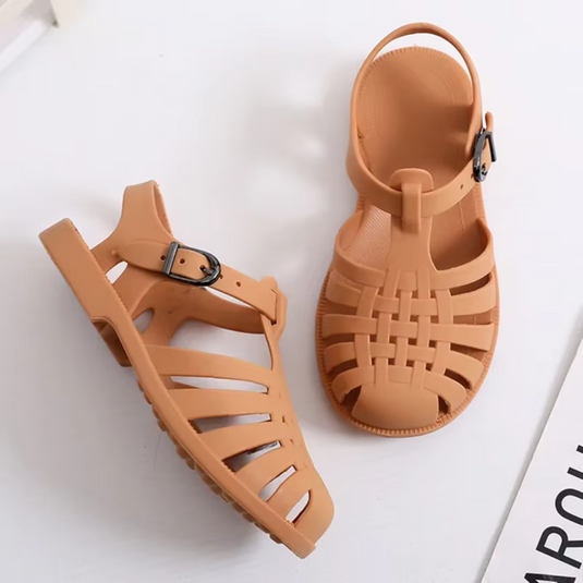 Braune Sandalen aus Kunststoff mit verstellbarem Riemen und geflochtenem Design auf weißem Hintergrund. Ideal für Sommermode und Strand.