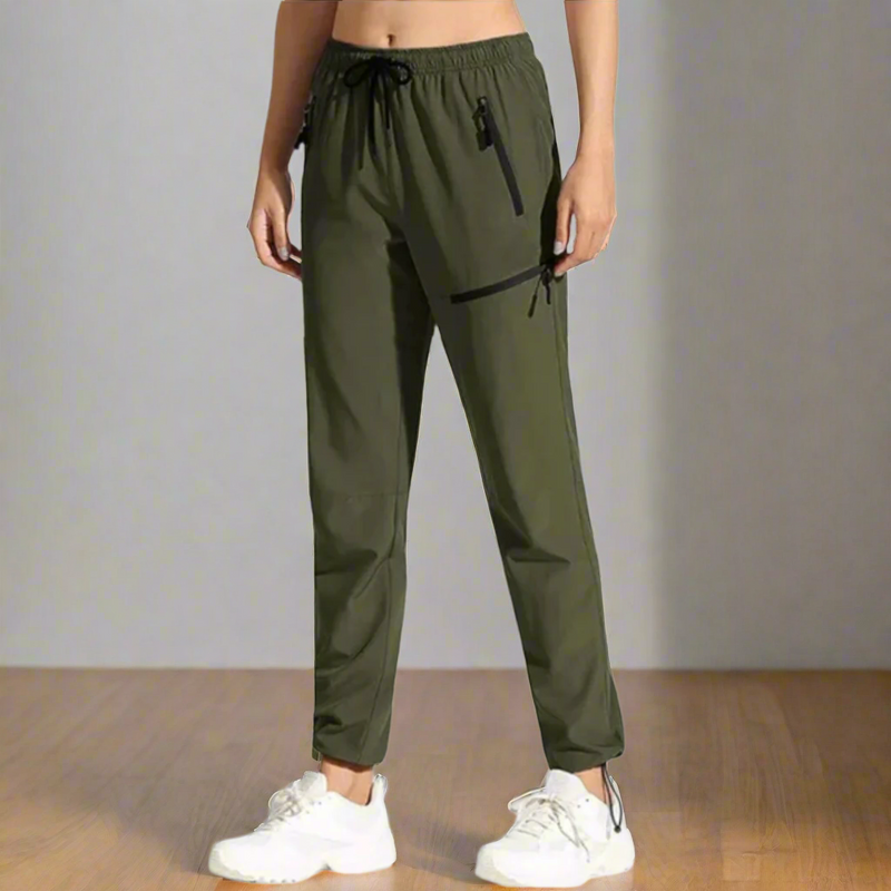 Laden Sie das Bild in Galerie -Viewer, Damen in olivgrüner Jogginghose mit Kordelzug und weißen Sneakers auf Holzboden. Sportliche Freizeitmode, bequeme Damenbekleidung.
