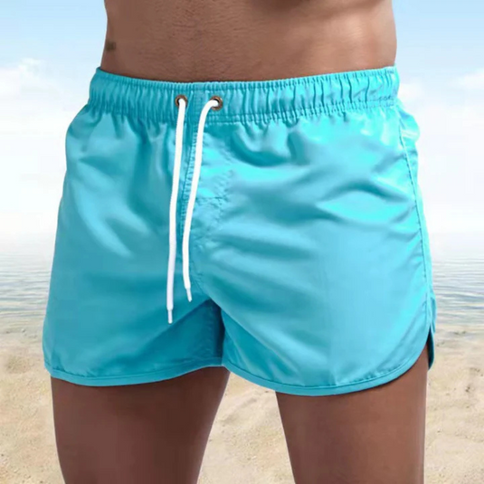 Mann in türkisblauer Badehose am Strand, Sommermode, Herren-Bademode, Strandbekleidung, Urlaub, Meereshintergrund.