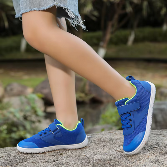 Blaue Kinderschuhe mit Klettverschluss, getragen von einem Kind auf einem Steinweg im Freien. Bequeme, sportliche Sneaker für Jungen und Mädchen.