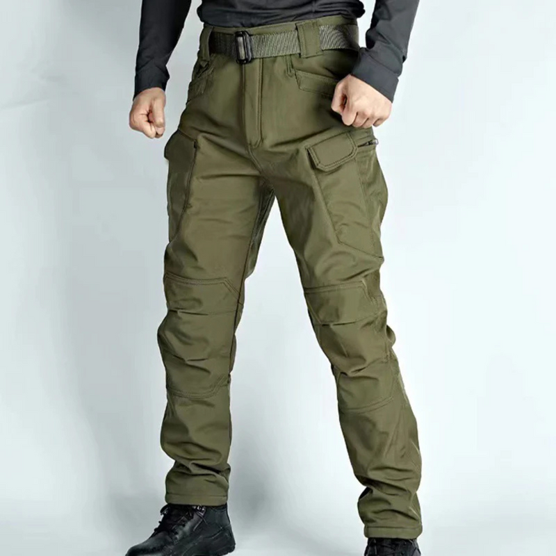 Laden Sie das Bild in Galerie -Viewer, Mann trägt olivgrüne taktische Hose mit mehreren Taschen, Gürtel und schwarzen Stiefeln. Outdoor-Bekleidung, strapazierfähig, funktional.
