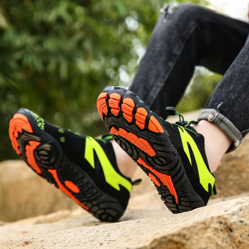 Laden Sie das Bild in Galerie -Viewer, Schwarze und neonfarbene Wanderschuhe mit orangefarbener Sohle auf Felsen; Outdoor-Schuhe, rutschfest, ideal für Trekking und Abenteuer.
