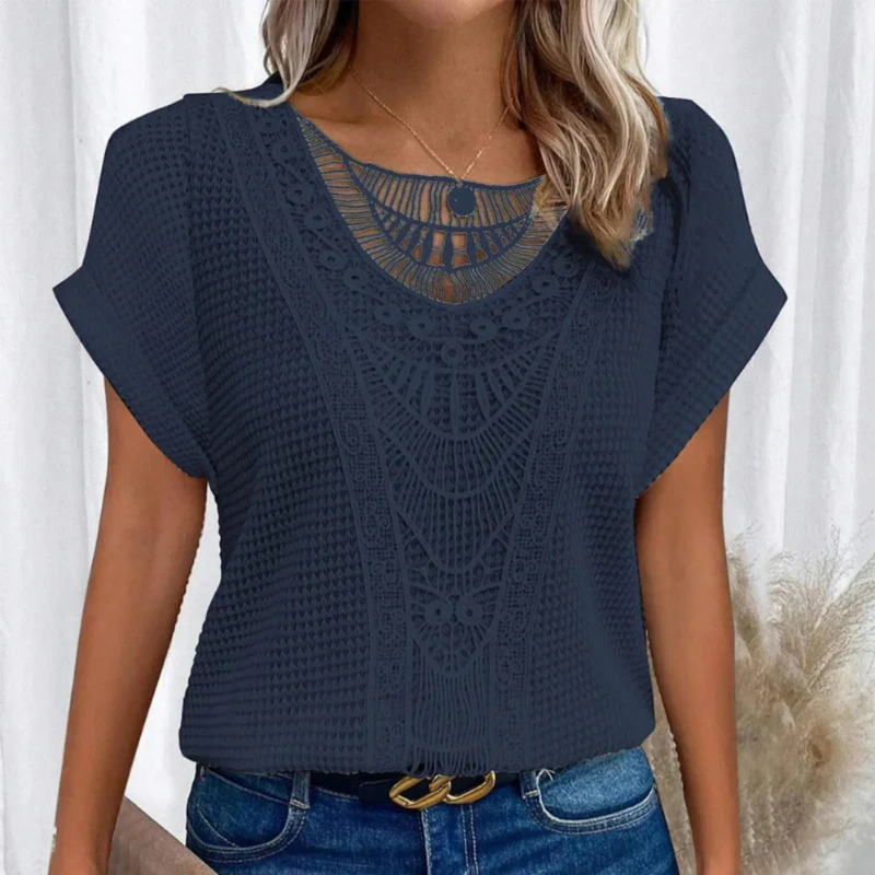 Laden Sie das Bild in Galerie -Viewer, Frau trägt dunkelblaues Spitzenoberteil mit geometrischem Muster, kombiniert mit blauer Jeans. Modetrend, Damenmode, elegantes Design.
