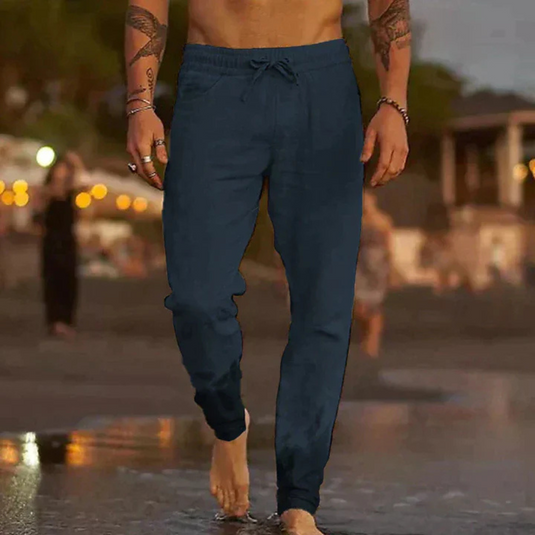 Mann in blauer Jogginghose geht barfuß am Strand entlang, Abendstimmung, Freizeitkleidung, entspannte Atmosphäre, Sommermode.