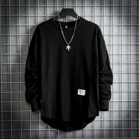 Schwarzes Langarmshirt mit Kettenanhänger, hängend vor grauem Gitterhintergrund. Modisches Herrenoberteil, urbaner Streetwear-Stil.