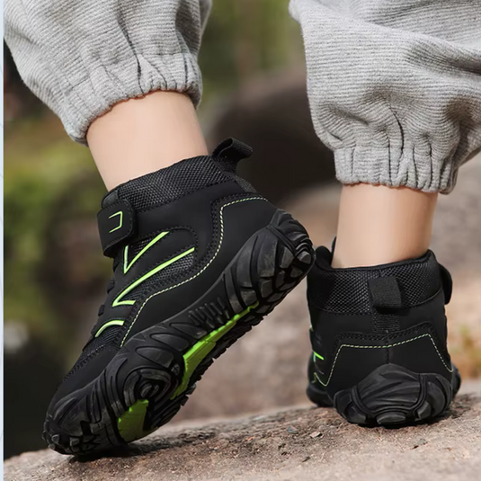 Schwarze Kinder-Wanderschuhe mit grünen Akzenten, robuste Sohle, graue Jogginghose, Outdoor-Abenteuer, rutschfest, bequem, langlebig.
