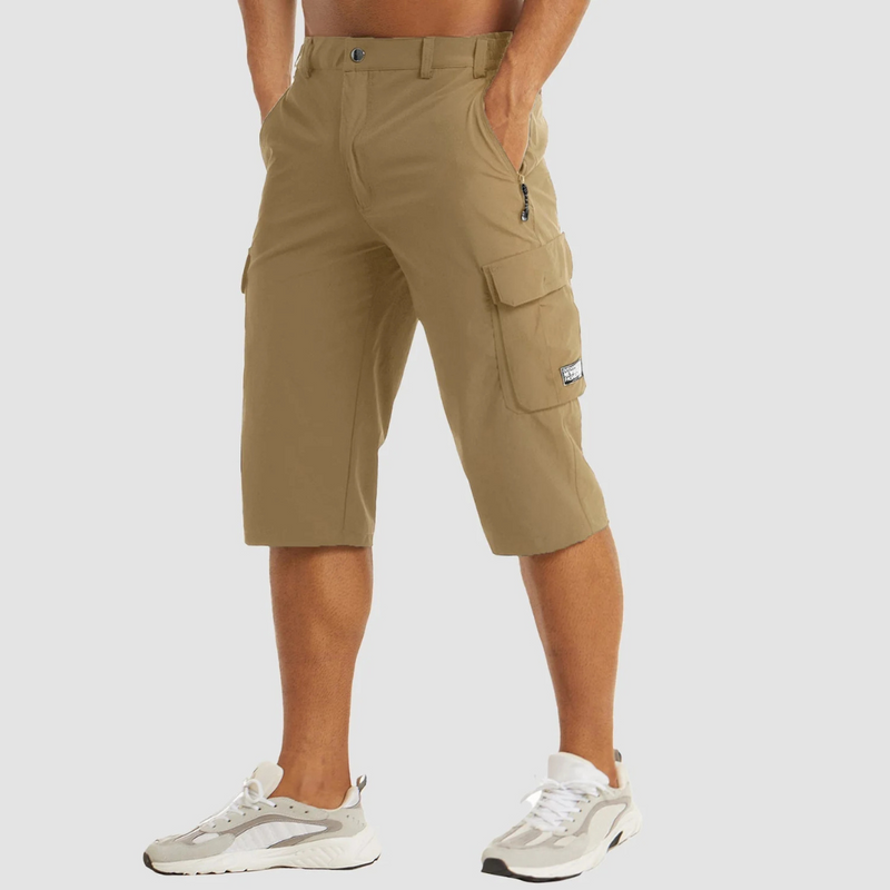 Laden Sie das Bild in Galerie -Viewer, Beige Cargo-Shorts für Herren, knielang, mit Seitentaschen und Reißverschluss, kombiniert mit weißen Sportschuhen. Ideal für Outdoor-Aktivitäten.
