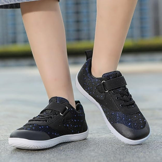 Schwarze Kindersneaker mit blauen Punkten, Klettverschluss und weißer Sohle auf grauem Boden. Bequeme, modische Schuhe für Kinder.