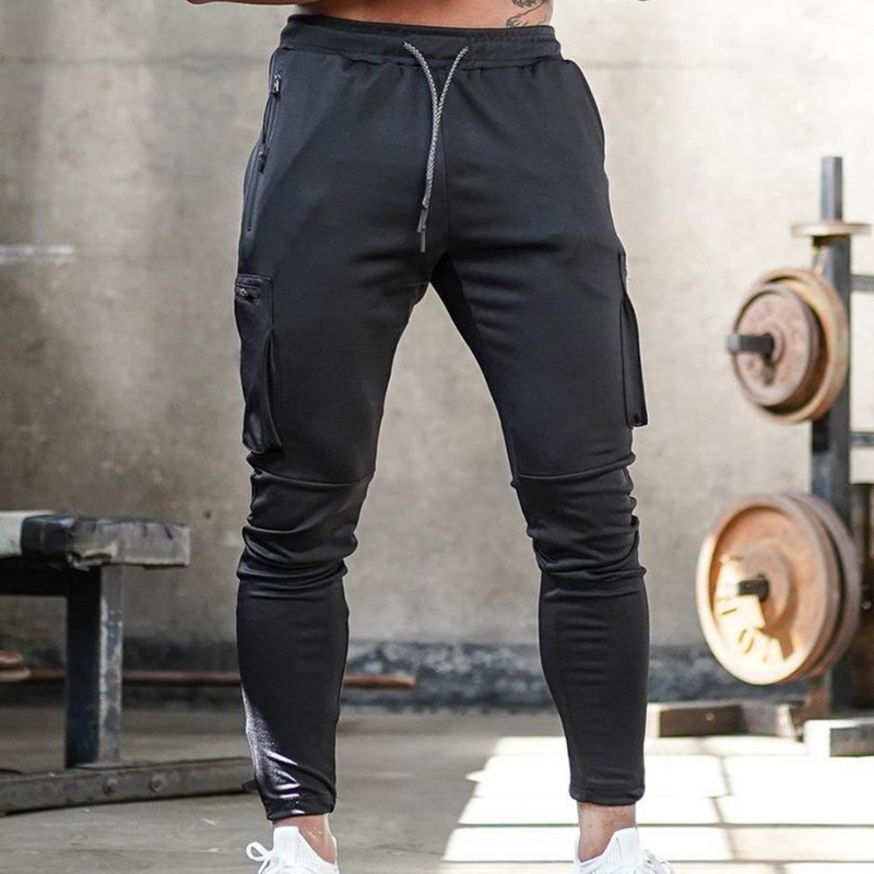 Laden Sie das Bild in Galerie -Viewer, Schwarze Jogginghose mit Taschen, getragen in einem Fitnessstudio. Sportliche Herrenmode, ideal für Training und Freizeit. Bequeme Passform.
