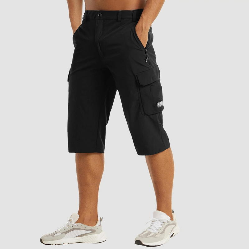 Laden Sie das Bild in Galerie -Viewer, Schwarze Cargo-Shorts für Herren, knielang, mit Seitentaschen und Reißverschluss, kombiniert mit weißen Sneakers. Ideal für Freizeit und Outdoor.
