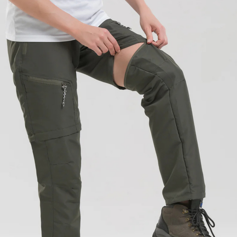 Laden Sie das Bild in Galerie -Viewer, Person trägt olivgrüne, abnehmbare Outdoor-Hose mit Reißverschluss, ideal für Wandern und Trekking. Praktische, wandelbare Funktionshose für Abenteuer.
