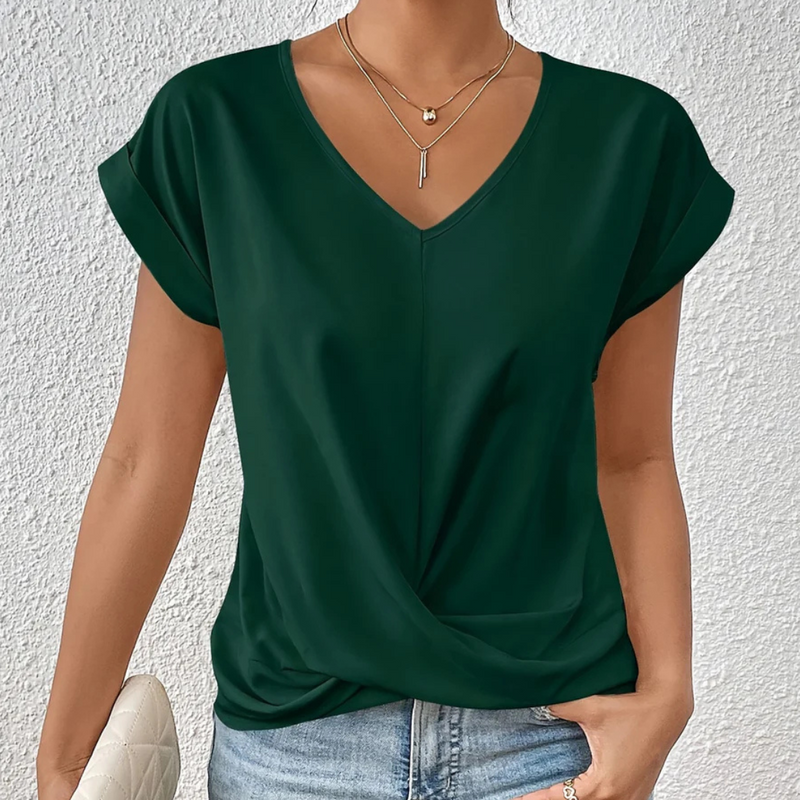 Laden Sie das Bild in Galerie -Viewer, Frau trägt dunkelgrünes V-Ausschnitt-Shirt, kombiniert mit blauer Jeans und goldener Halskette, vor weißer Wand. Elegante Damenmode, Freizeitlook.
