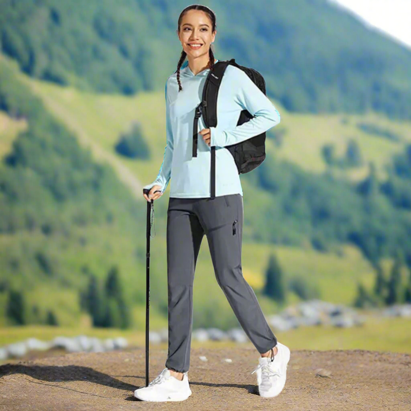 Laden Sie das Bild in Galerie -Viewer, Frau beim Wandern in den Bergen, trägt hellblauen Hoodie, graue Hose, Rucksack und Wanderstock. Outdoor-Aktivität, Natur, Fitness.
