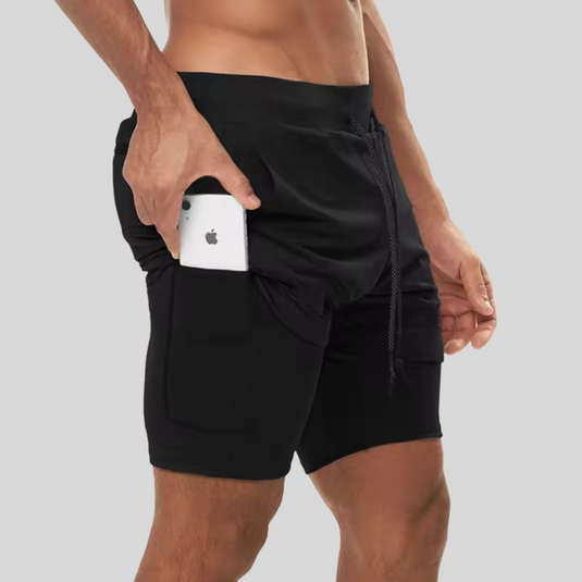 Mann in schwarzen Sportshorts mit Smartphone-Tasche, hält ein Smartphone. Ideal für Fitness, Laufen, Training. Bequeme, funktionale Sportbekleidung.