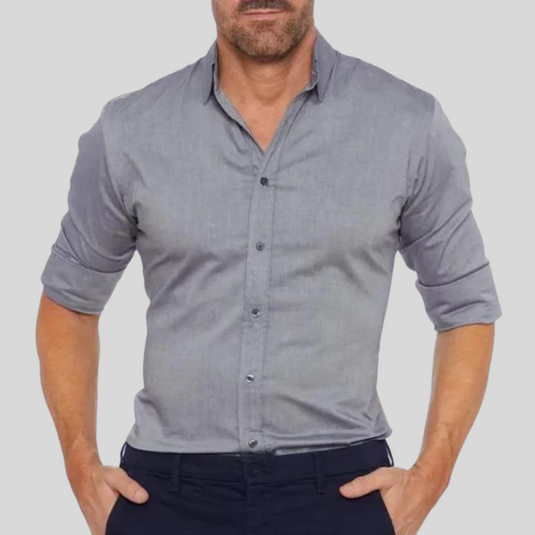 Mann in grauem Hemd mit hochgekrempelten Ärmeln, Hände in Hosentaschen. Elegante Herrenmode, Freizeitlook, stilvolles Outfit.