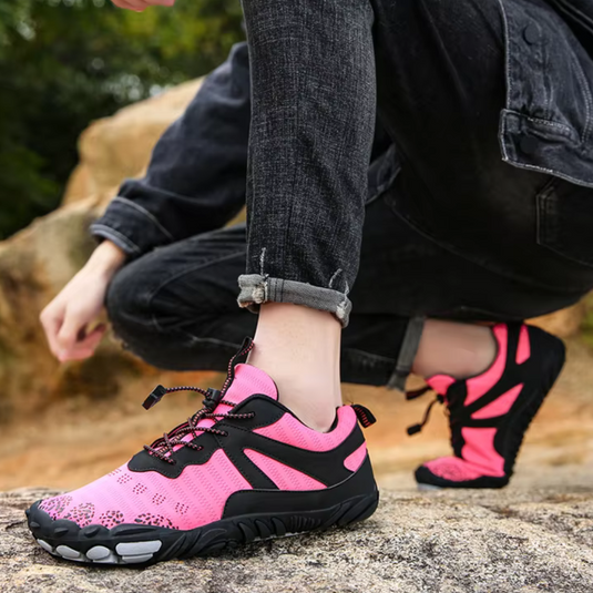 Person trägt pinke und schwarze Outdoor-Schuhe auf Felsen, ideal für Wandern und Trekking. Bequeme, rutschfeste Sportschuhe für Damen und Herren.