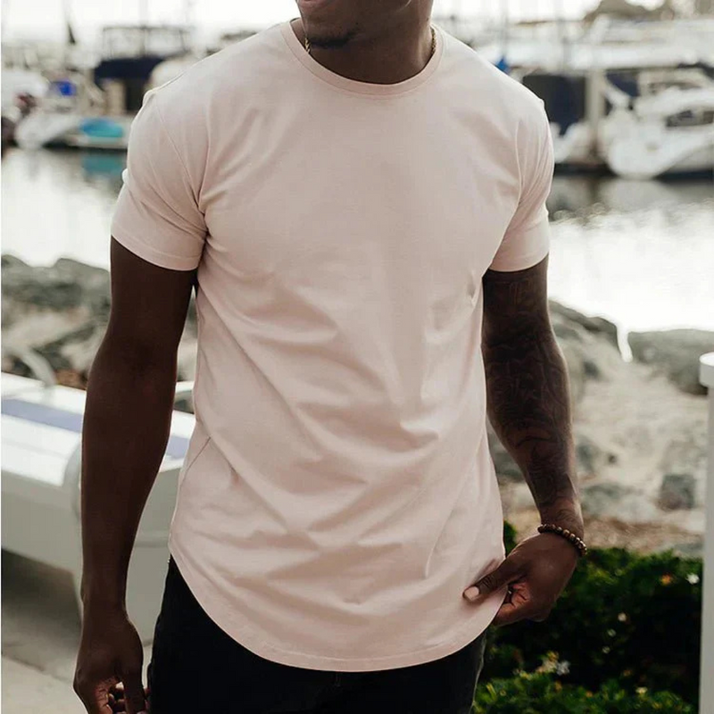 Laden Sie das Bild in Galerie -Viewer, Mann in beigem T-Shirt am Hafen, Boote im Hintergrund. Sommermode, Freizeitkleidung, stilvoll, lässig, maritimes Ambiente.
