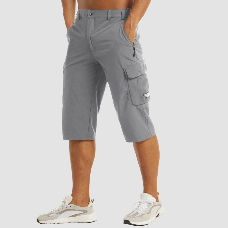 Laden Sie das Bild in Galerie -Viewer, Graue Cargo-Shorts für Herren, knielang, mit Seitentaschen und Reißverschluss, kombiniert mit weißen Sneakers. Ideal für Freizeit und Outdoor.
