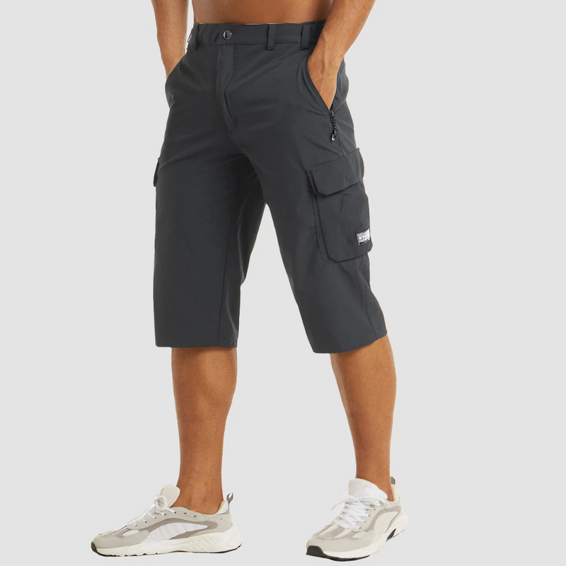 Laden Sie das Bild in Galerie -Viewer, Mann trägt schwarze Cargo-Bermudashorts mit Taschen, kombiniert mit weißen Sneakers. Modische Sommerkleidung für Herren, ideal für Freizeit und Outdoor.

